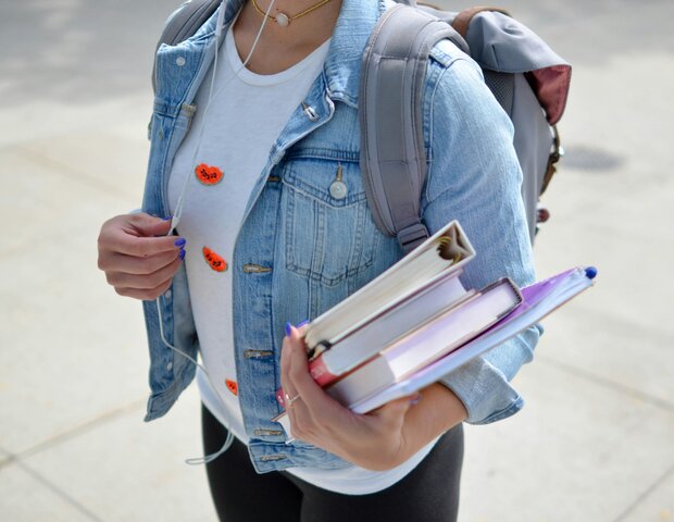 Eine Schülerin in Jeansjacke hält Schulbücher in der Hand